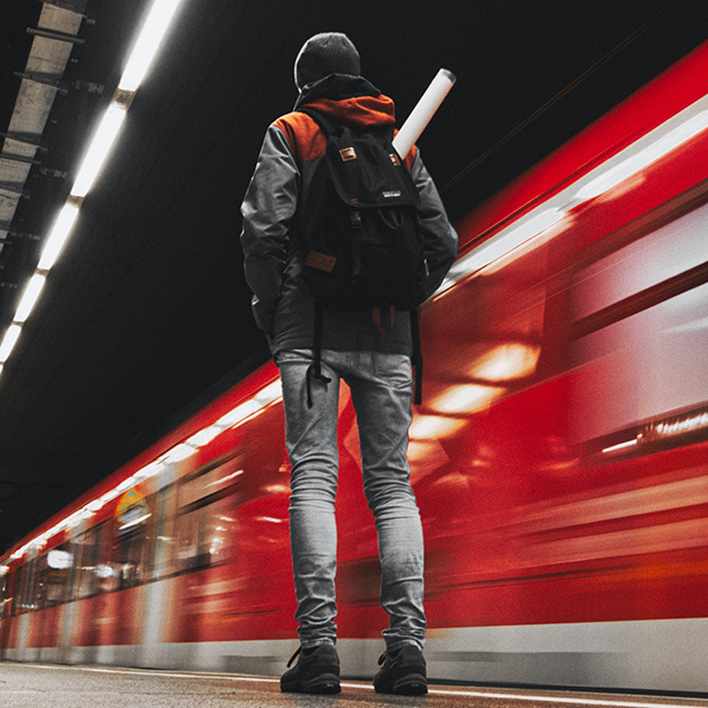 Eine Person läuft mit einem Rucksack auf einem Bahnsteig an aneme vorbeifahrenden Zug vorbei