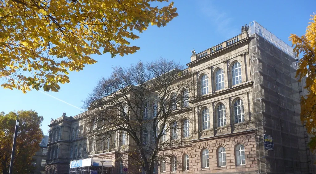 Historisches Hauptgebäude der RWTH Aachen mit Herbstbäumen im Vordergrund.