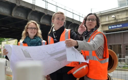 Bauzeichnerinnen und Ingenieure besprechen Baupläne auf einer Baustelle.