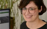 Portrait von Ulrike Hunscha lächelnd und freundlich vor einem Bürohintergrund.