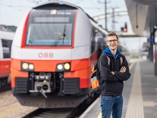 Lokführerin steht vor einem roten Zug auf dem Bahnsteig und lächelt.