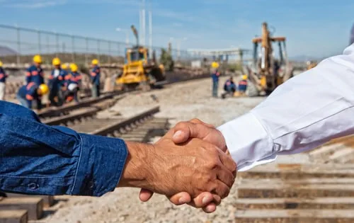 Händedruck zwischen zwei Personen auf einer Baustelle symbolisiert Partnerschaft.