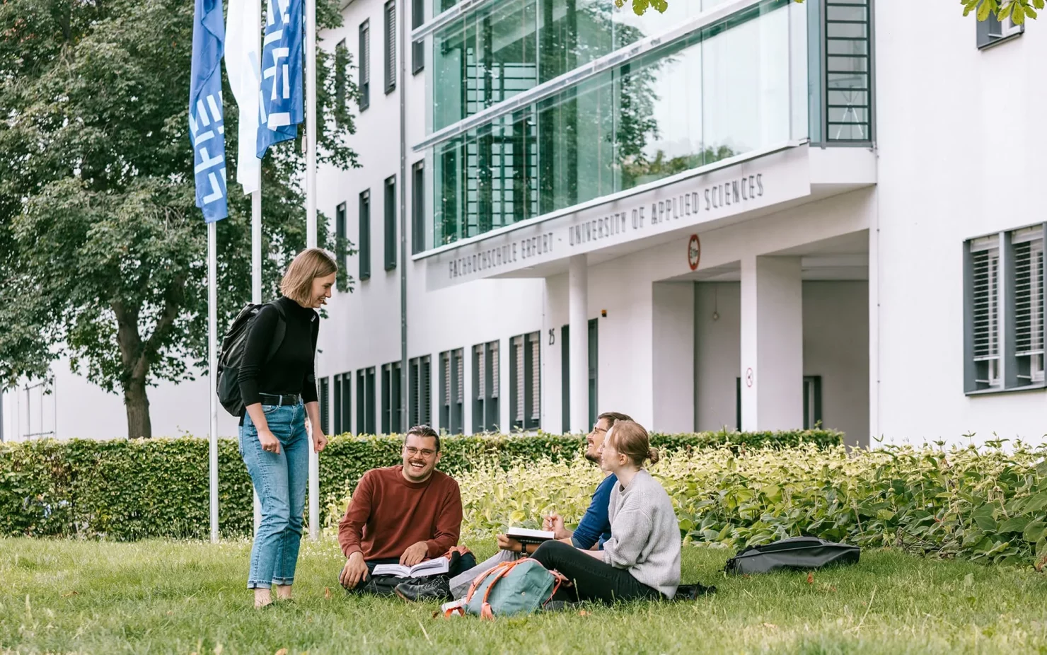 Studierende sitzen auf einer Wiese vor einem Gebäude auf dem Campus der FH Erfurt.