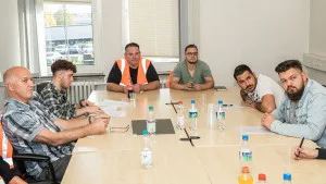 Gruppe von Personen in einem Besprechungsraum darunter ein Mann in Warnkleidung.